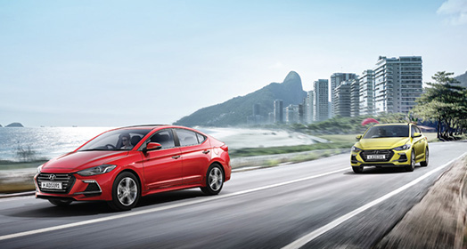 Left side front view of two Elantra Sport cars driving on the road with the city background