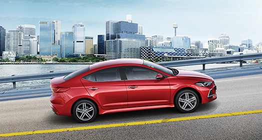 Side view of red Elantra Sport on the road with buildings background